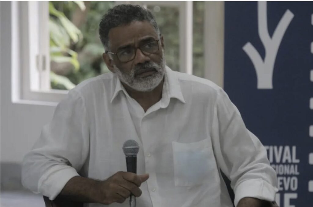 Hombre mayor con camisa blanca hablando en micrófono